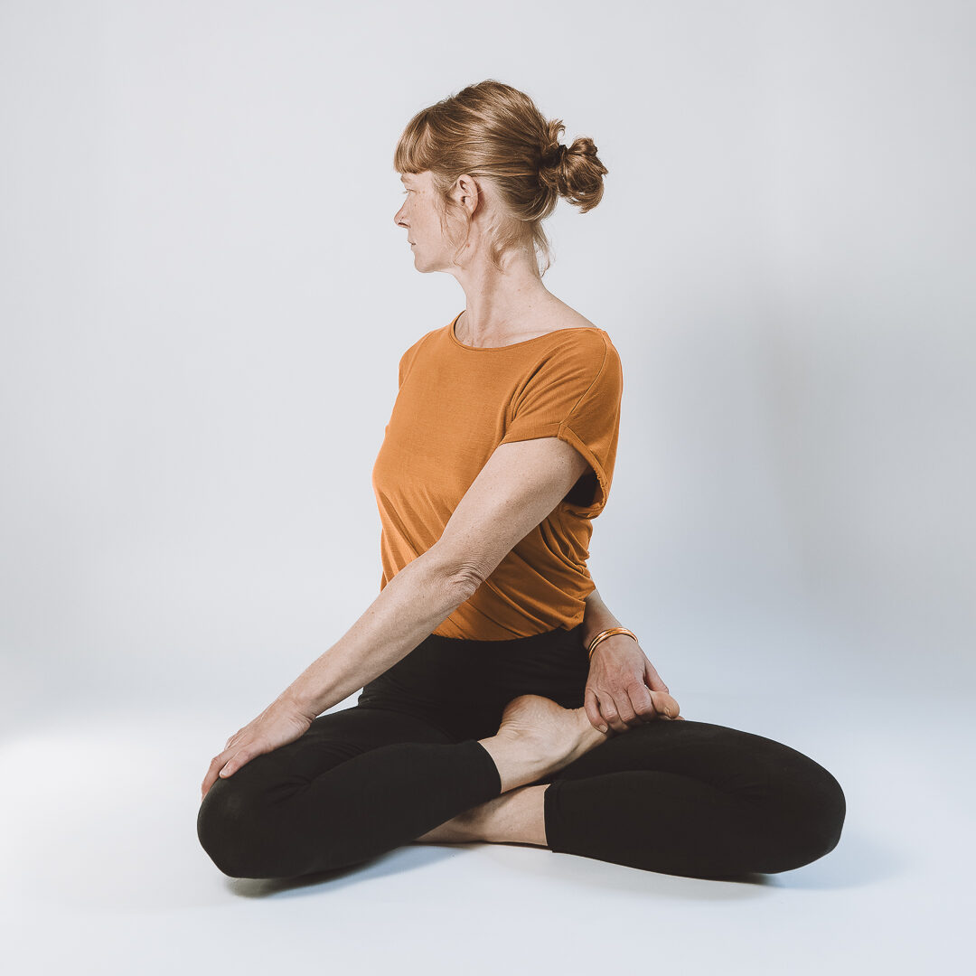 posture assise de torsion sur fond blanc dans une tenue orange