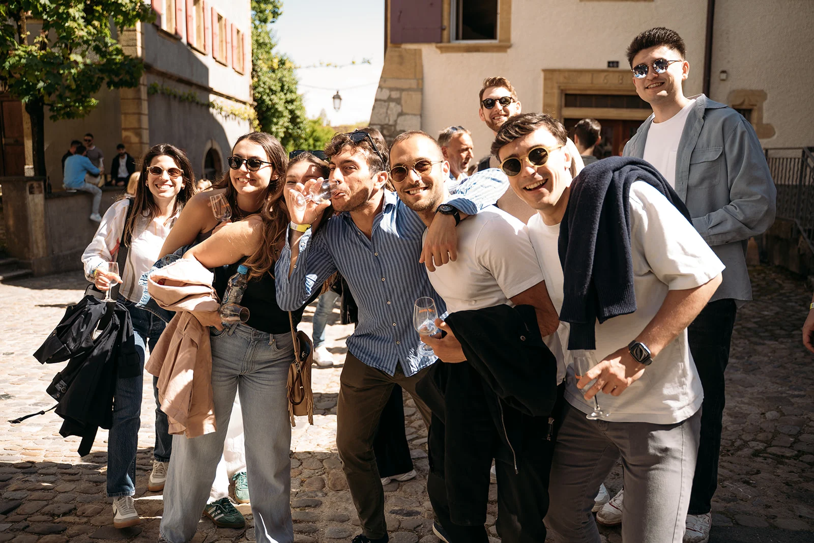 Groupe de jeunes adultes souriants lors des Caves Ouvertes 2025 à Neuchâtel, en plein cœur du village sous un soleil printanier.
