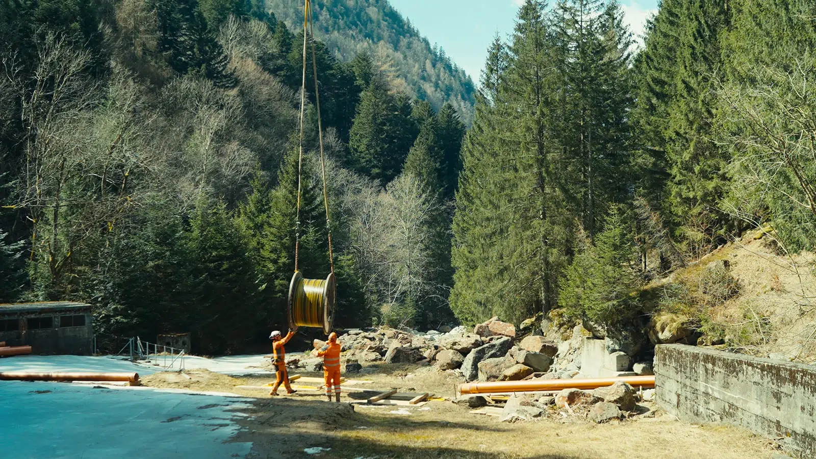 Transport de câbles électriques en pleine nature, au bord d’une rivière dans les Alpes tessinoises.