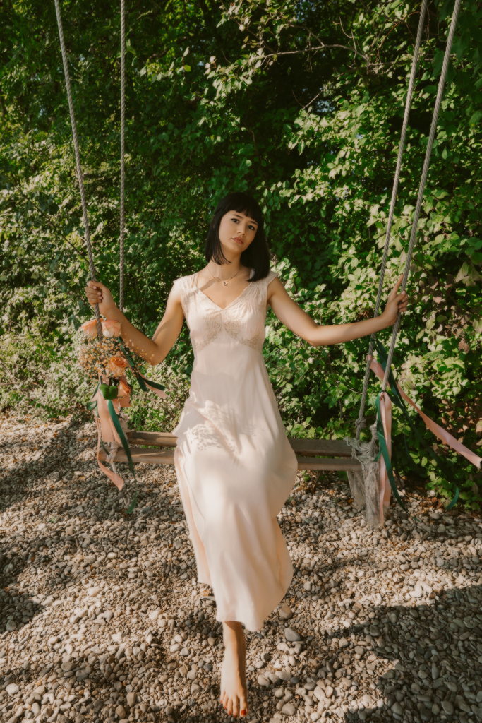 Modèle portant une robe poudrée et des bijoux Diane Gem’s by Alice Leloir sur une balançoire au bord du lac, photo de Sarah Adatte