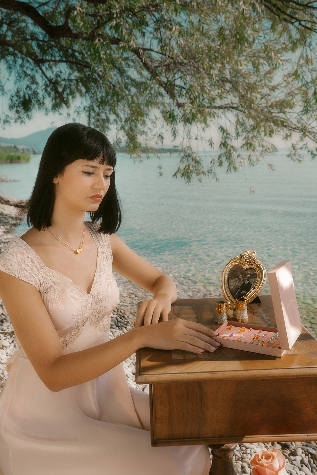 Océane K portant un collier Diane Gem’s by Alice Leloir, assise au bord du lac de Neuchâtel avec une boîte de bijoux ouverte, photo de Sarah Adatte